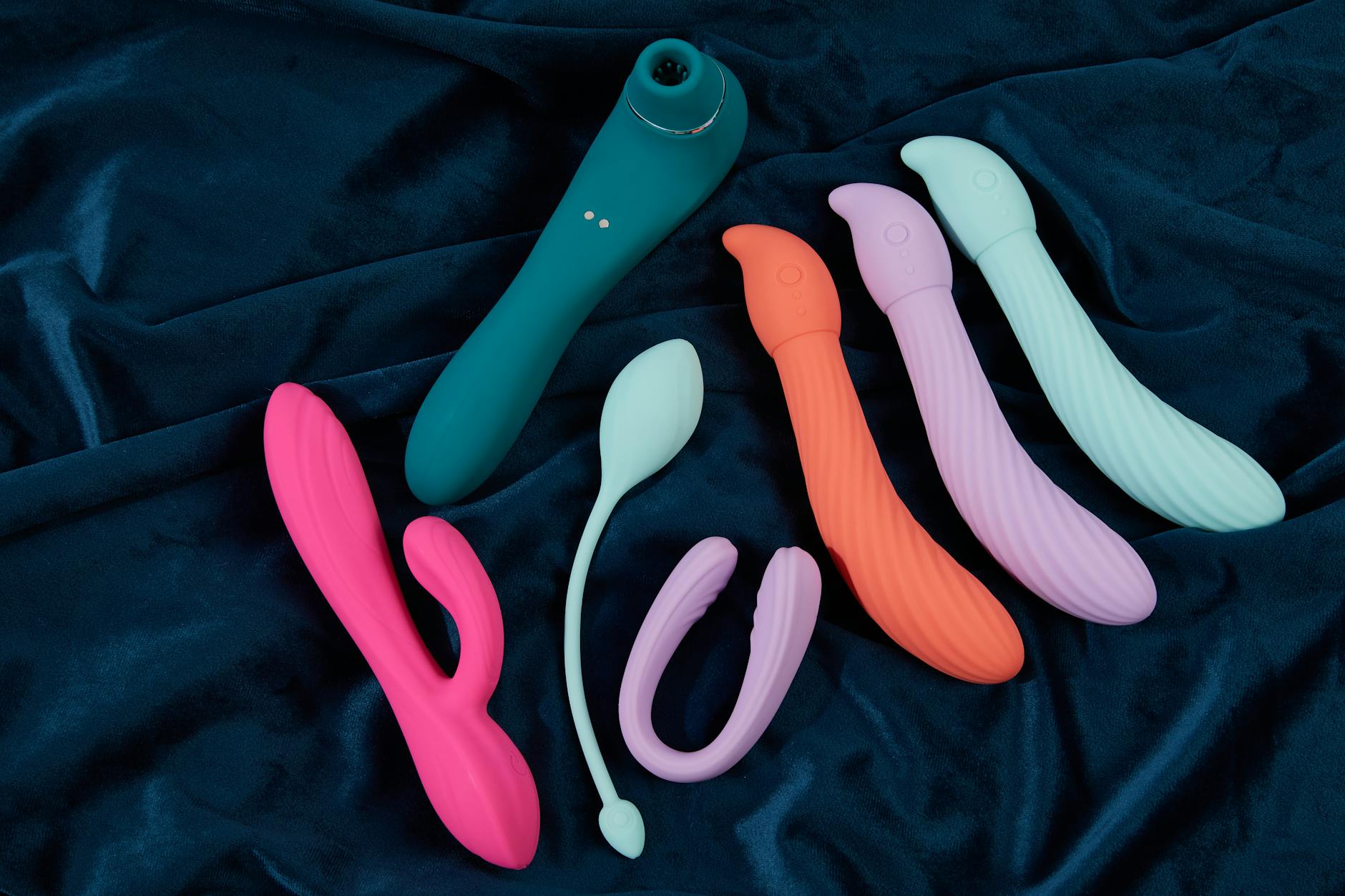 Collection of colorful silicone vibrators on dark fabric, representing diverse pleasure tools