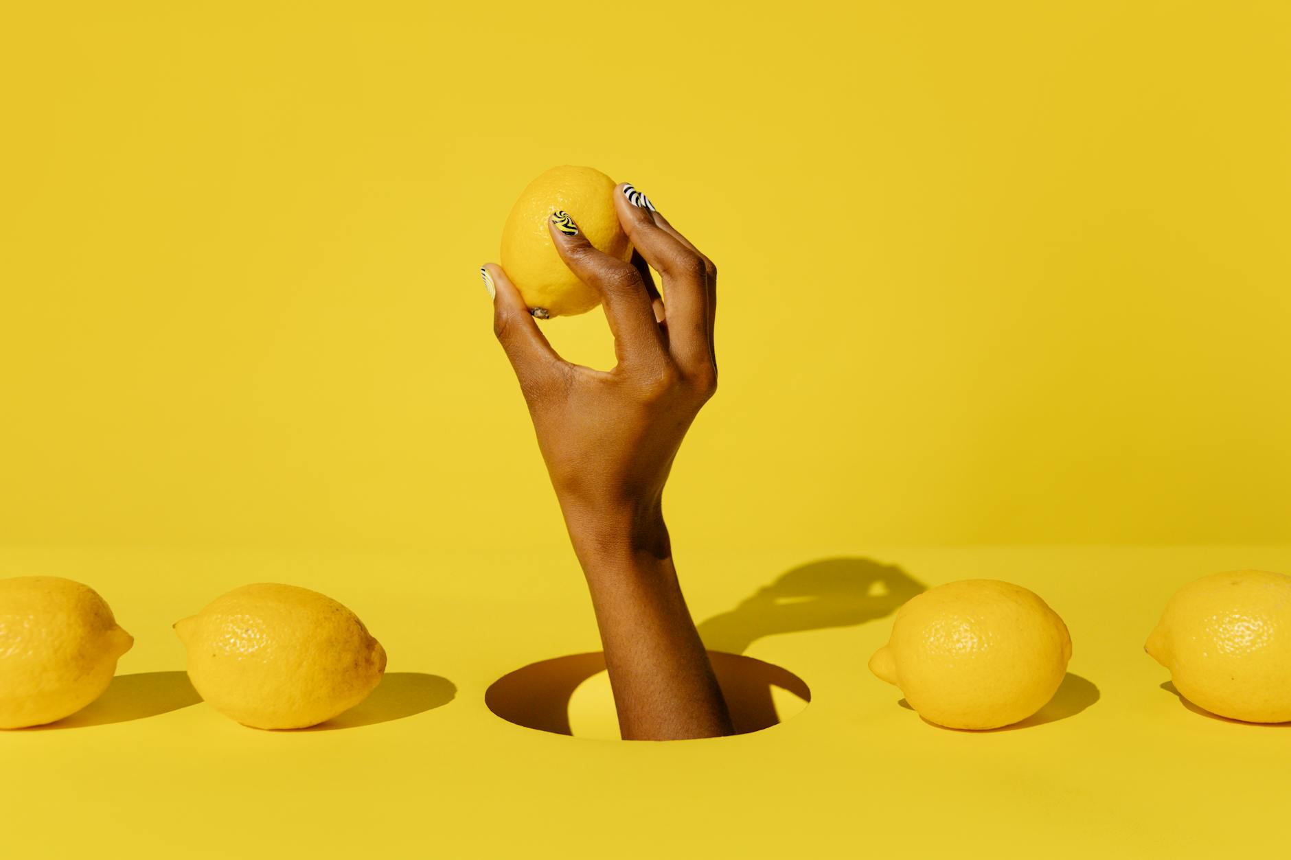 Hands holding a sleek lemon clitoral vibrator against a purple background