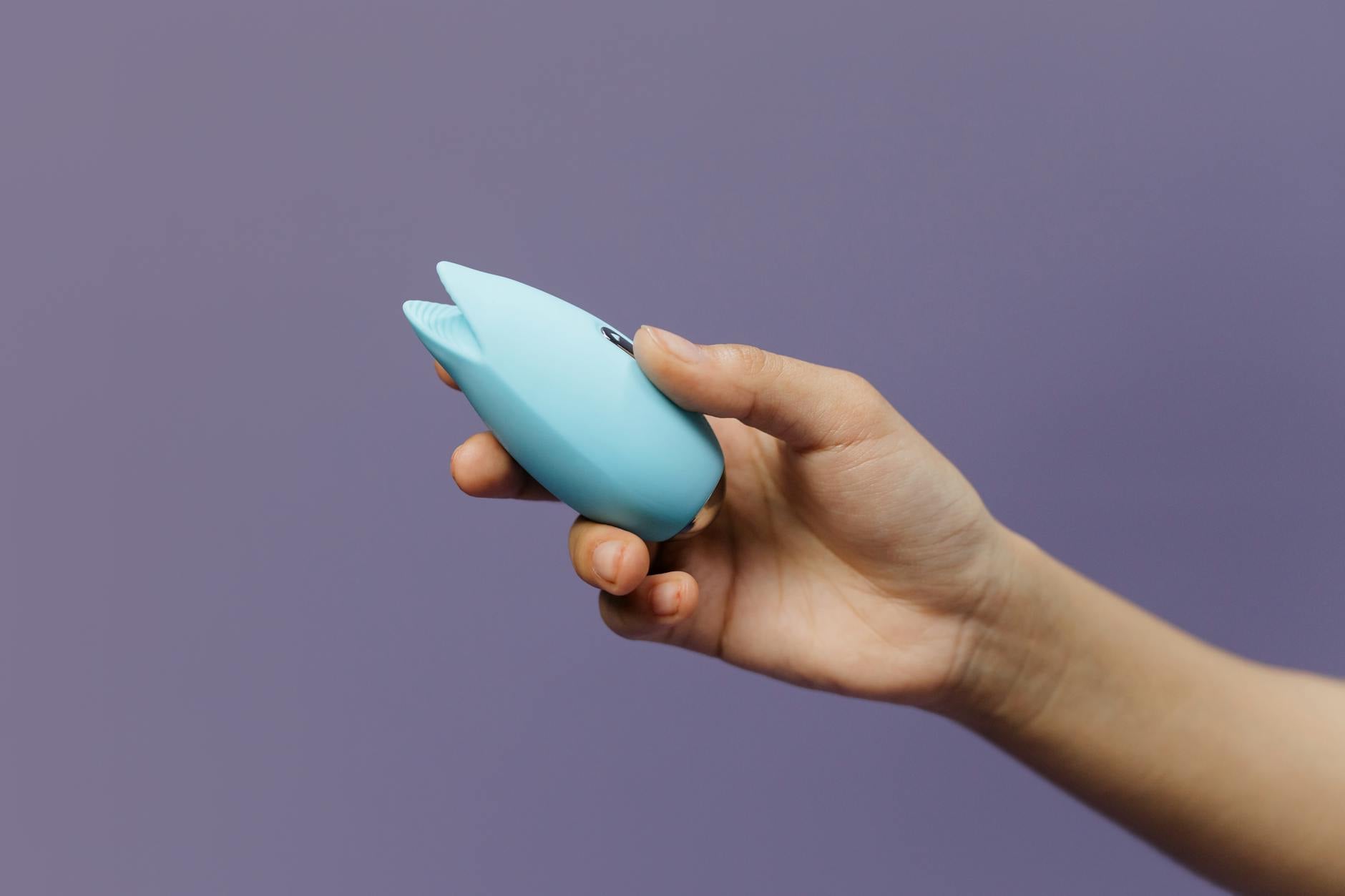 A blue clitoral vibrator held in hand against a purple background, representing modern pleasure recovery
