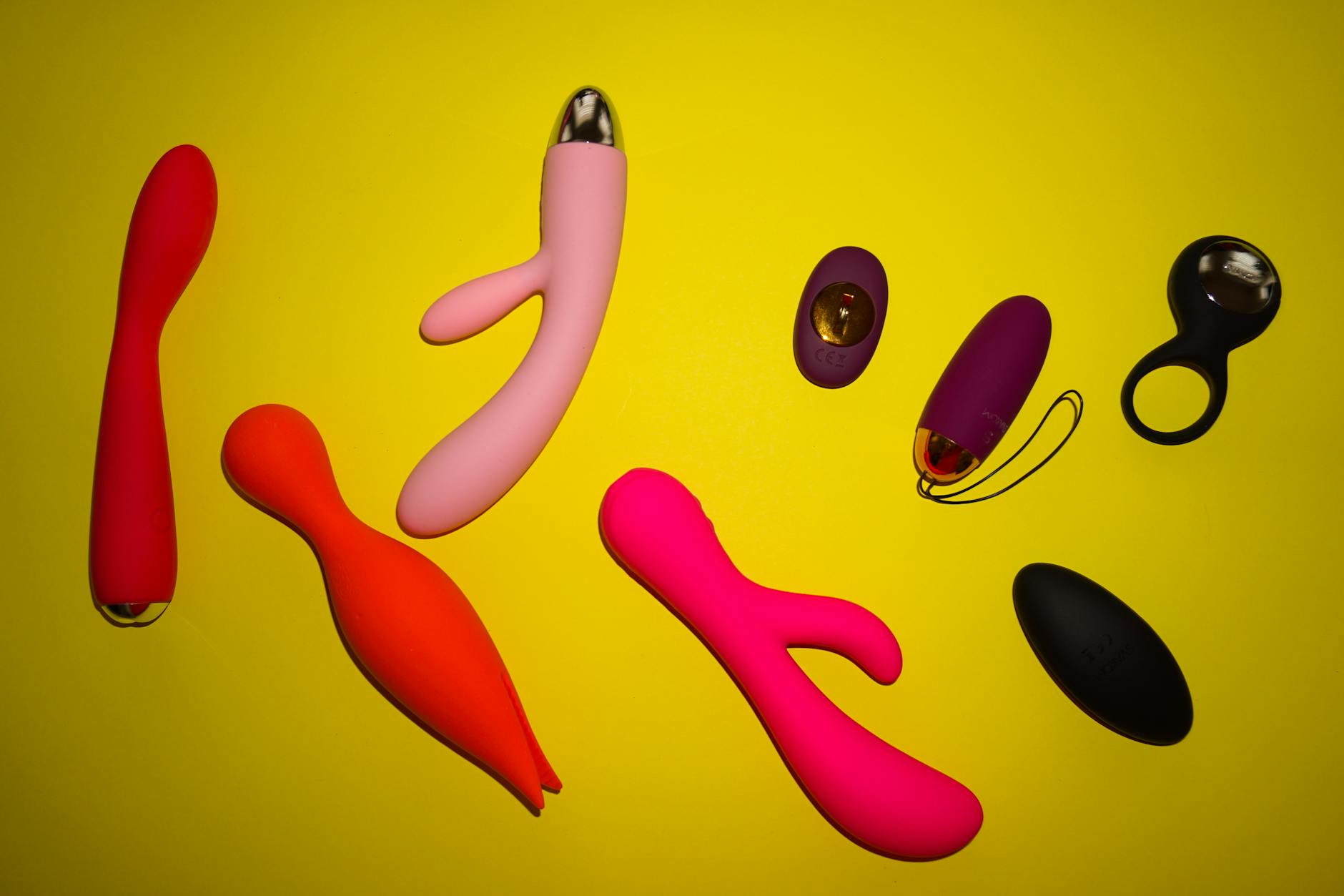 Vibrant collection of colorful sex toys on bright yellow surface, representing diverse approaches to pleasure and connection