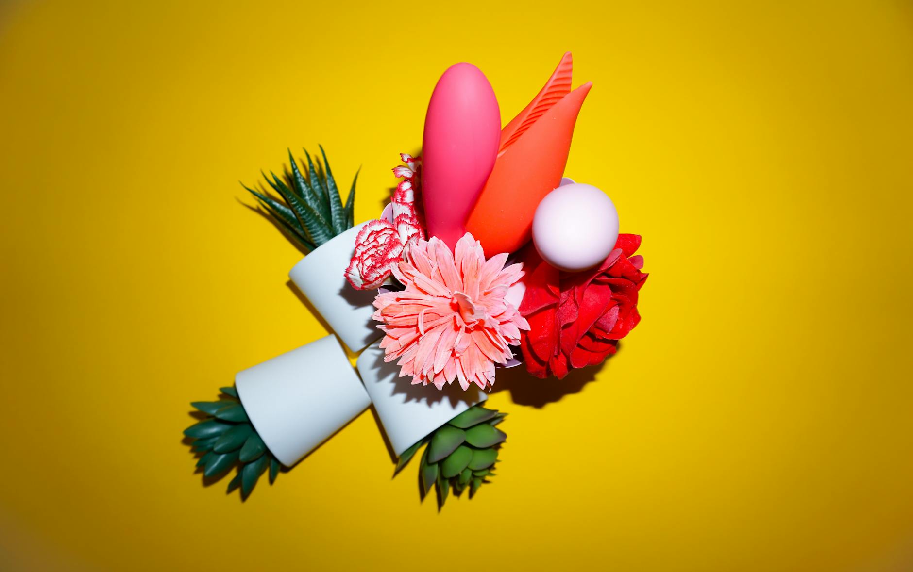 Two hands holding pink and blue silicone vibrators against a pastel background